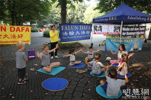 '图5：二零二一年八月二十一日，法轮功学员在慕尼黑的霍亨索伦广场（Hohenzollernplatz）举办活动。一群小朋友和一位德国妇女带着孩子一起跟学员学炼打坐。'