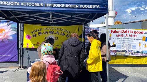 图2：在赫尔辛基闹市区，人们驻足“法轮大法日”庆祝活动真相展位