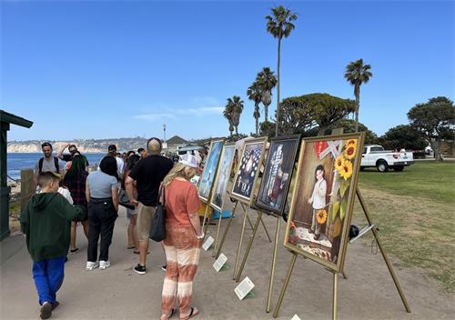 '图4：二零二二年五月七日，圣地亚哥学员在拉荷雅（La Jolla）海边洪法讲真相，“真善忍美展”的画作吸引游人驻足观看。'