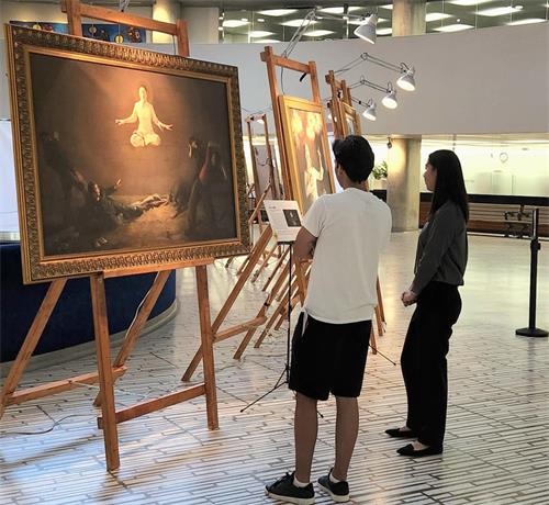 图11：雷（Ray左）在认真观赏画展。他表示很难想象在中共的统治下，有多少人面临着残酷的迫害。