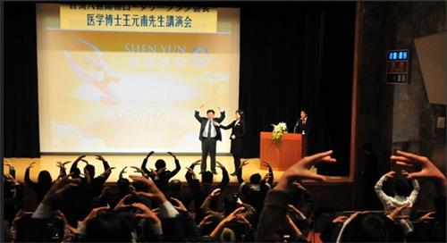 圖4：二零一二年一月十四日，王元甫在東京新宿的會堂演講「不花錢、不吃藥的氣功健康法」。圖為，王元甫在講台上演示法輪功第二套功法——法輪樁法，台下與會者跟著學煉動作。