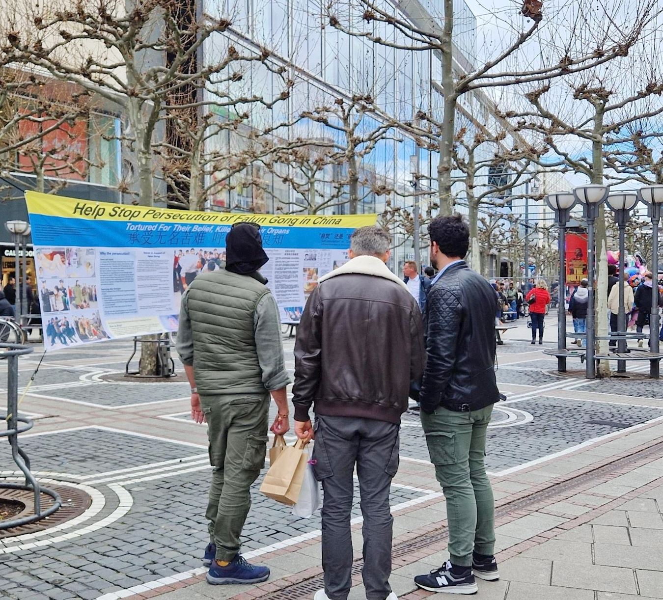'图1：二零二四年三月十六日，德国法兰克福的法轮功学员在市中心举办弘法活动，中英文的大型真相横幅吸引了过往的路人驻足观看。'