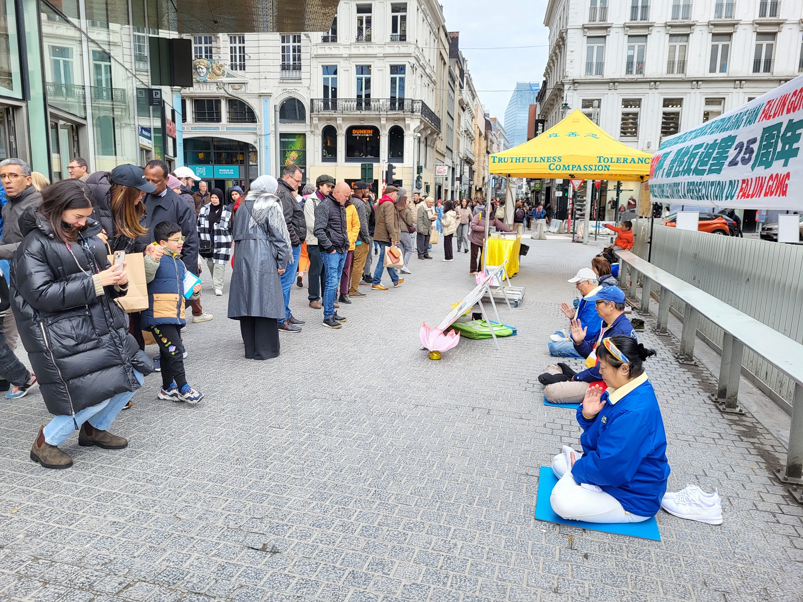 图1：二零二四年四月二十日，比利时法轮功学员在布鲁塞尔的商业大街旁举行纪念“四·二五”活动，并向市民展示法轮功功法。