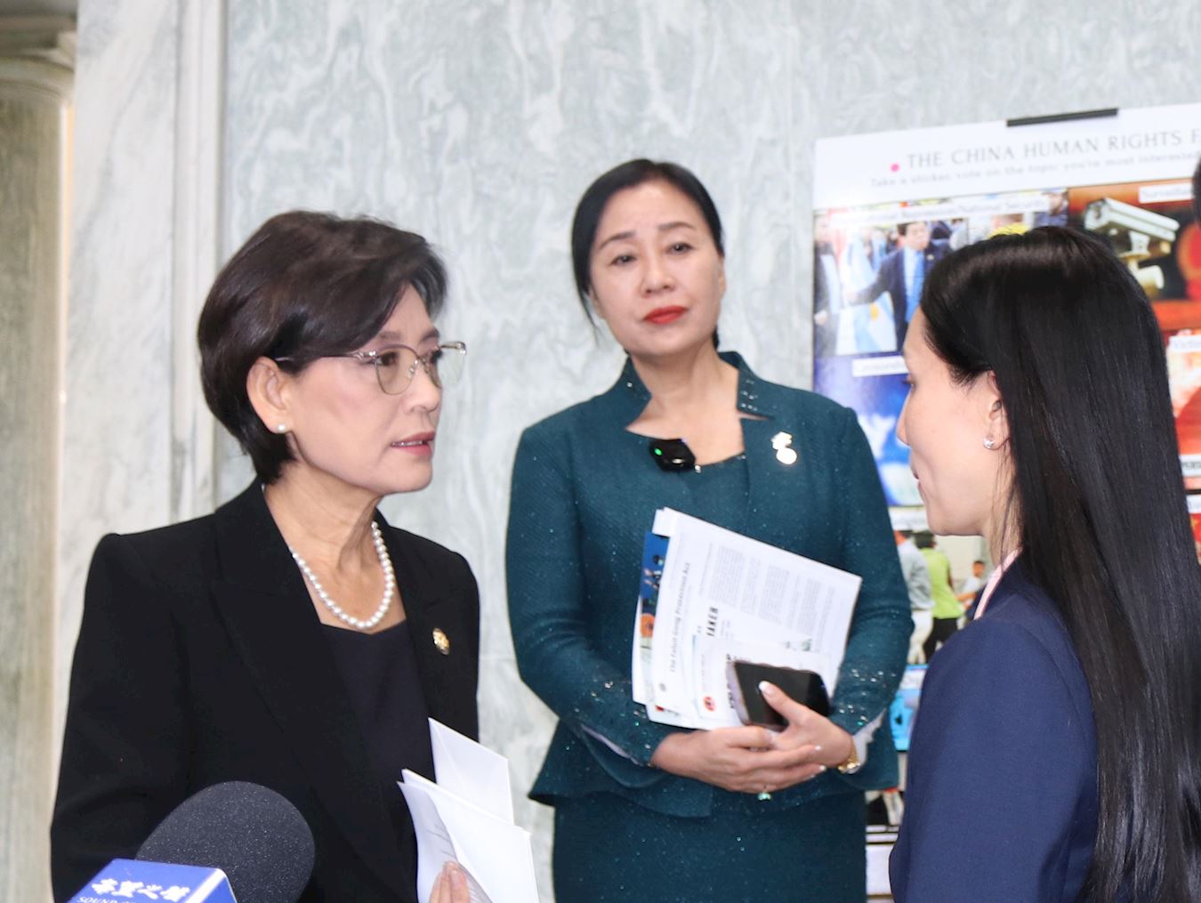 '图2:二零二五年十二月十日,法轮大法信息中心在美国国会主办人权展会,法轮功学员王珊珊(右一)向美国国会众议员金映玉(左一)讲述父母因修炼法轮功遭受中共迫害的经历。'